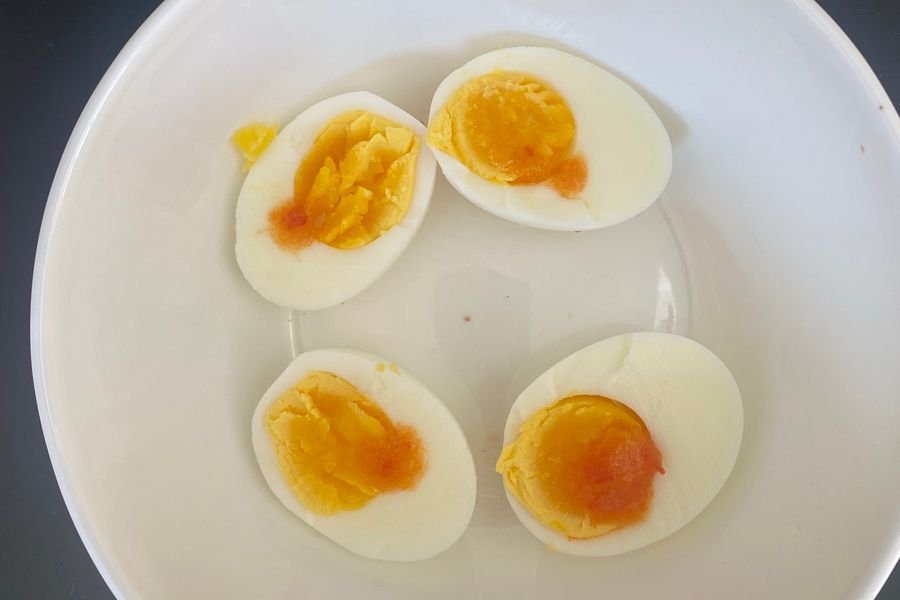 Four halves of medium boiled eggs in a white bowl, the yolks set at the edge and soft in the centre, topped with sea salt and hot sauce