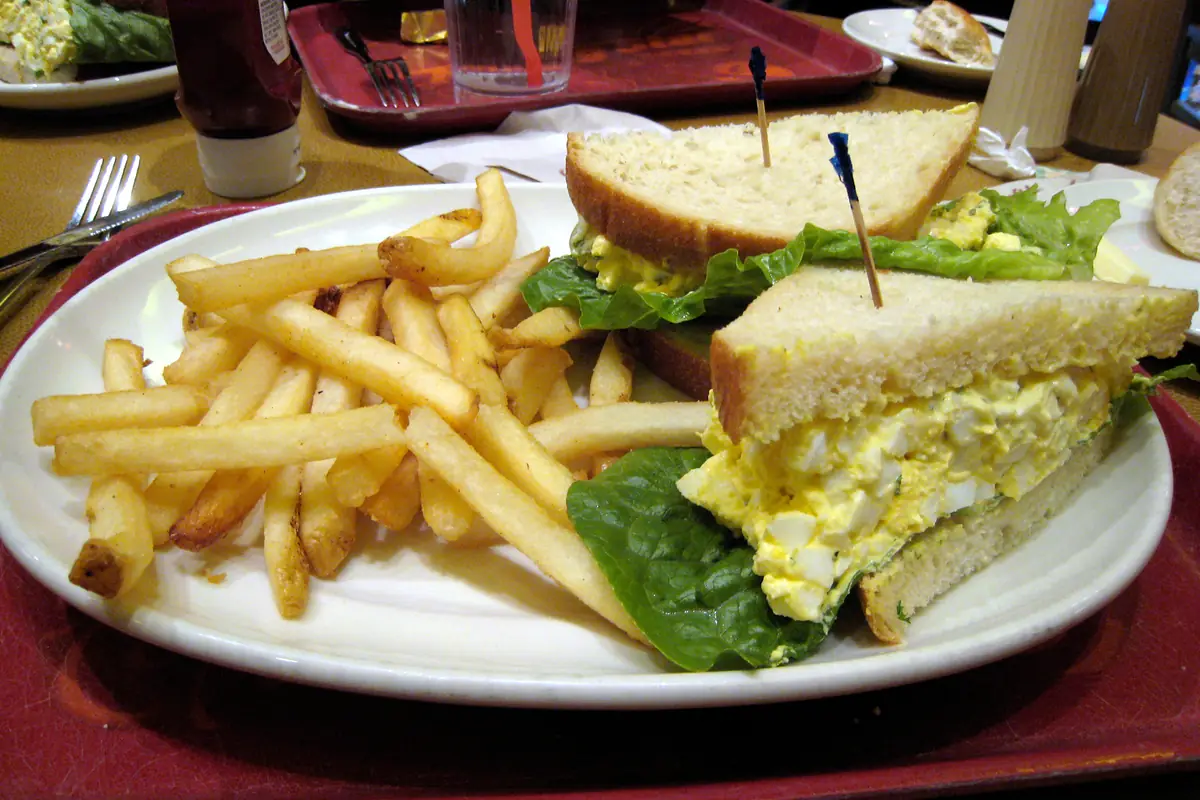 Egg salad sandwich cut in half on a plate with lettuce and fries