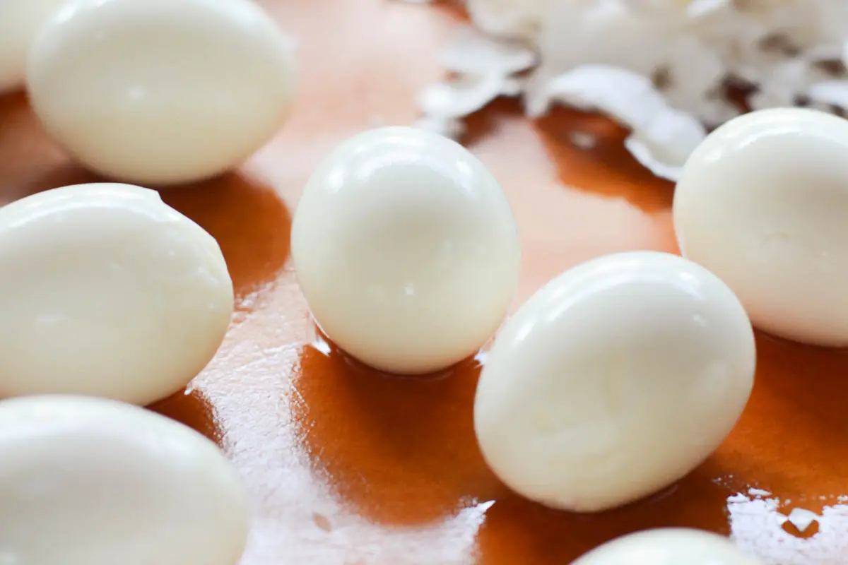 Peeled hard boiled eggs on a wooden board with pieces of shell nearby