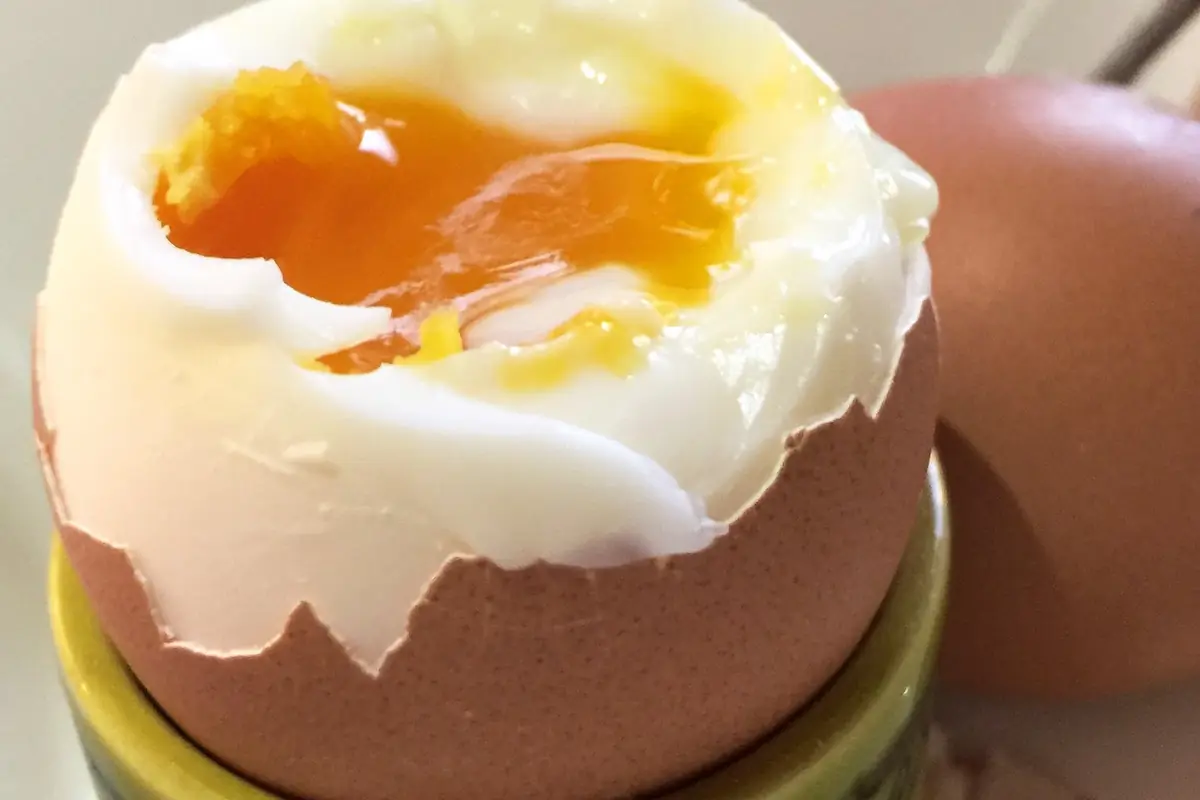 Soft boiled egg in an egg cup with the top cut off and a runny orange yolk